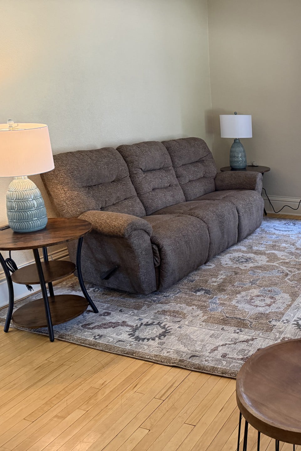 A brown sofa sits on a patterned rug between two wooden side tables, each with a lamp—creating a welcoming space reminiscent of the warmth found in homes that provide support for youth in Central Minnesota. The room has light walls and a hardwood floor.